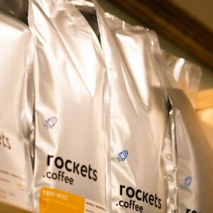 Home Close-up of branded coffee packs neatly arranged on a wooden shelf indoors.